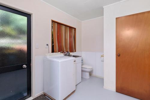 a bathroom with a toilet and a sink and a window at Serene at Snells - Snells Beach Bach in Snells Beach
