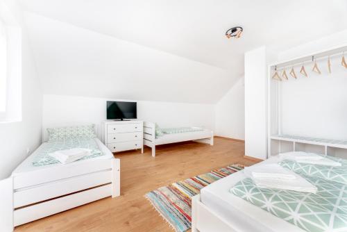 a white bedroom with two beds and a tv at Menta Porta in Zengővárkony