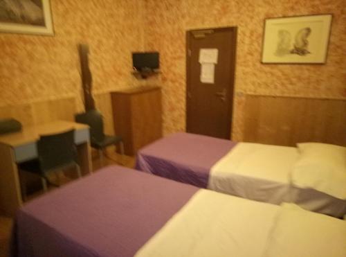 a hotel room with two beds and a table and a door at Hotel Ariosto centro storico in Reggio Emilia