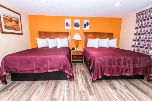two beds in a hotel room with orange walls at The Minuteman Inn Acton Concord Littleton in Acton