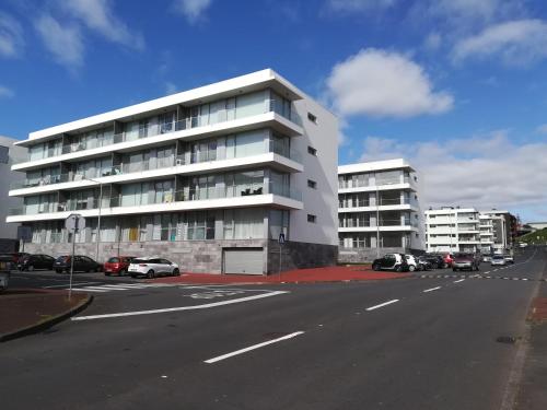 un grand bâtiment blanc avec des voitures garées dans un parking dans l'établissement Casa do Kiko, à Ponta Delgada