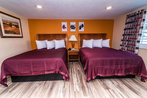 two beds in a hotel room with red sheets at The Minuteman Inn Acton Concord Littleton in Acton