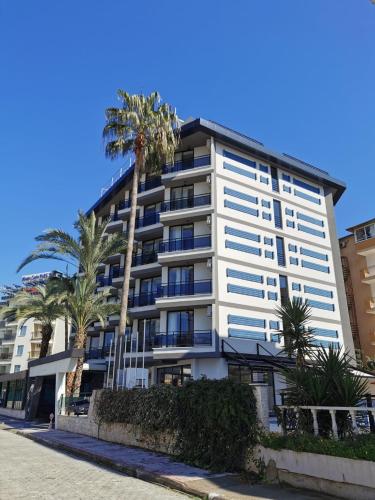 a tall white building with palm trees in front of it at Sette Serenity Hotel in Alanya