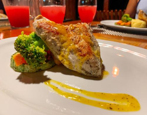 a white plate with a piece of chicken and broccoli at Las Caletas Lodge in Drake
