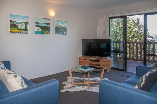 a living room with two blue chairs and a flat screen tv at Treetop Lodge - Acheron Holiday Home in Hanmer Springs