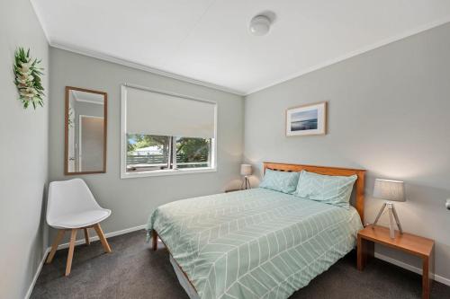 a bedroom with a bed and a window and a chair at Pohutukawa Breeze - Papamoa Beach Holiday Home in Papamoa