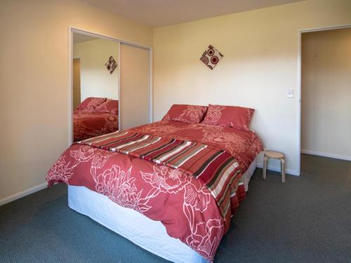 a bedroom with a bed with red sheets and a mirror at Rue Noyer Lookout - Akaroa Holiday Home in Akaroa