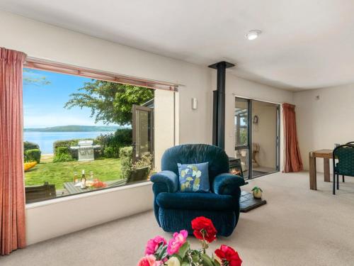 a living room with a blue chair and a large window at Mokoia Sunrise - Lakefront Ngongotaha Holiday Home in Ngongotaha