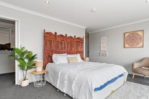 a white bedroom with a large bed and a chair at Sunrise, Seaviews and BBQs-Papamoa Beach Apartment in Papamoa