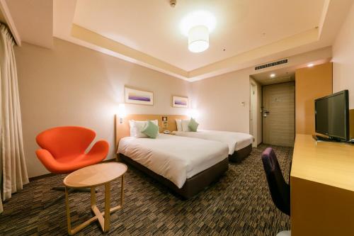 a hotel room with two beds and a chair at Hotel Resol Trinity Sapporo in Sapporo