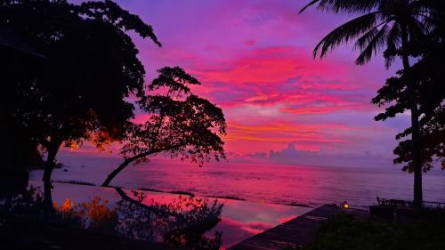 una puesta de sol sobre el océano con árboles en el primer plano en Jeeva Klui Resort, en Senggigi 