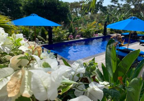 a pool at a resort with white flowers and blue umbrellas at Tatak Bunut Villa Ceningan in Nusa Lembongan