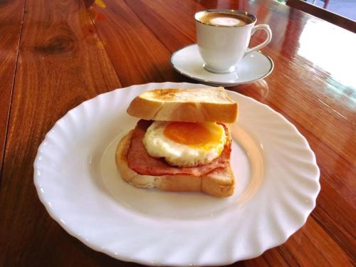 a breakfast sandwich on a white plate with a cup of coffee at Urban Hostel Bangkok in Bangkok
