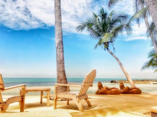 a beach with two chairs and palm trees at Sibaja Palms Sunset Beach Luxury Apartments in Taling Ngam Beach