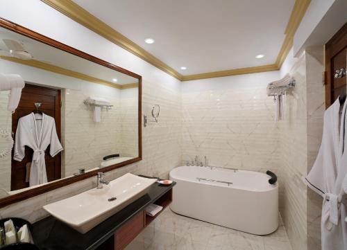 ein Badezimmer mit einer Badewanne, einem Waschbecken und einem Spiegel in der Unterkunft Mayfair Heritage in Puri