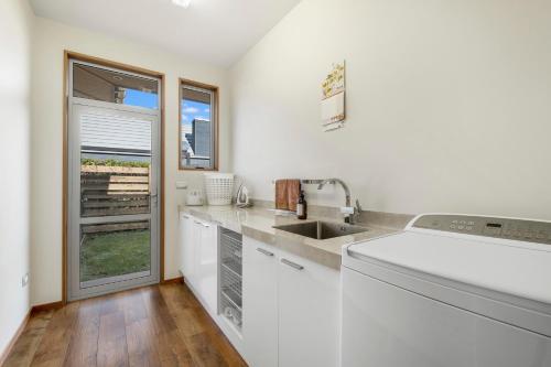eine Küche mit weißen Schränken und einer Spüle und einem Fenster in der Unterkunft Infinity Views - Modern Wanaka Holiday Home in Wanaka