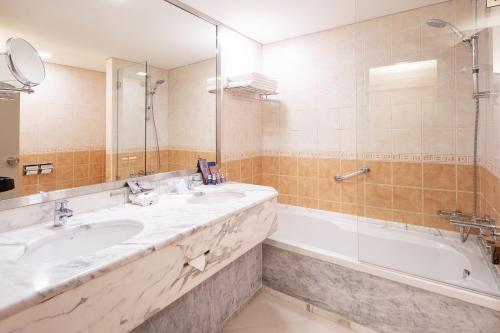 La salle de bains est pourvue de 2 lavabos et d'une baignoire. dans l'établissement Occidental Sharjah Grand, à Charjah