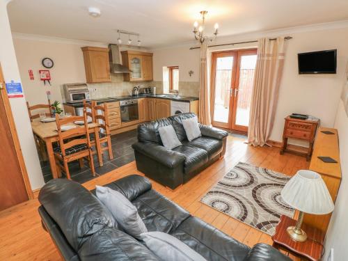 a living room with a leather couch and a kitchen at The Dairy in Llanmorlais