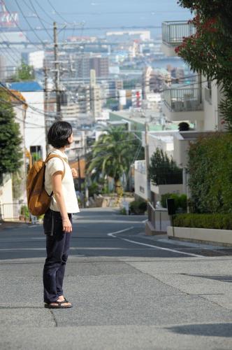 a woman with a backpack standing on a street looking at a city at Kobe Guesthouse MAYA in Kobe
