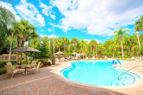a pool at a resort with tables and chairs and palm trees at Best Western Plus Kissimmee-Lake Buena Vista South Inn & Suites in Kissimmee