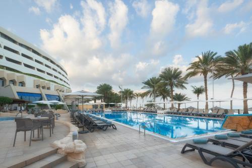 uma piscina de resort com mesas, cadeiras e palmeiras em Occidental Sharjah Grand em Sharjah