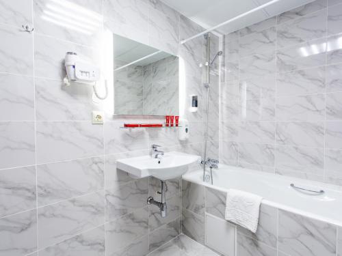 a white bathroom with a sink and a bath tub at AZIMUT Hotel Kemerovo in Kemerovo