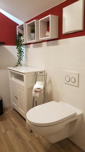 a bathroom with a white toilet and a red wall at Kleine gemütliche Mansardenwohnung im Südosten Münchens in Aßling