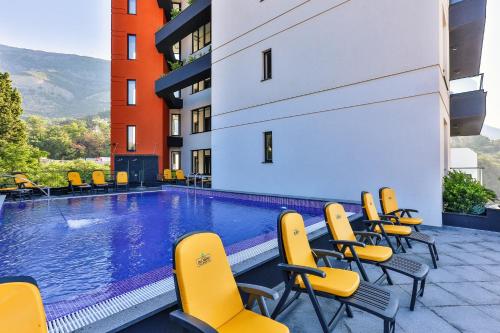 a swimming pool with yellow chairs and a building at Hotel Del Medio in Sutomore