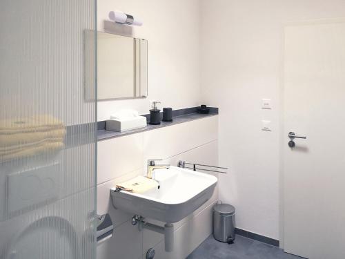 a white bathroom with a sink and a mirror at Atrium Apartments in Schaffhausen