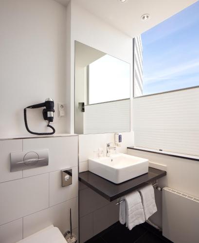 a white bathroom with a sink and a mirror at Webers - Das Hotel im Ruhrturm in Essen