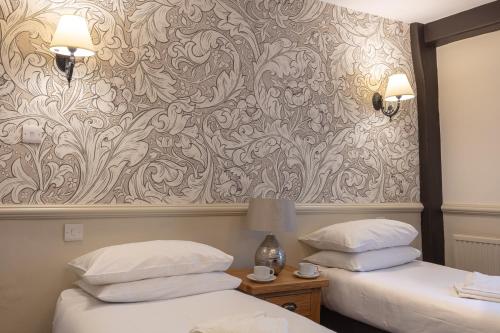 two beds in a hotel room with a wallpaper at The New Inn by Roomsbooked in Gloucester