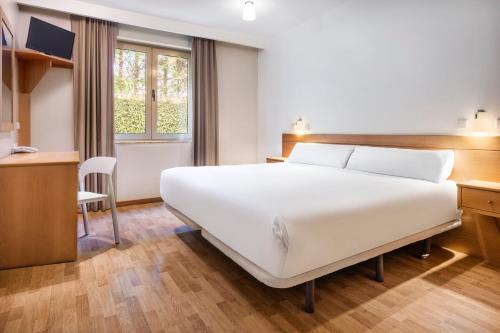 een slaapkamer met een groot wit bed en een bureau bij B&B HOTEL Braga Lamacaes in Braga