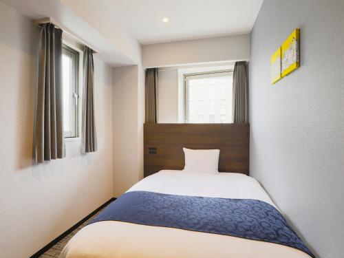 a small bedroom with a bed and two windows at Hotel Wing International Ikebukuro in Tokyo