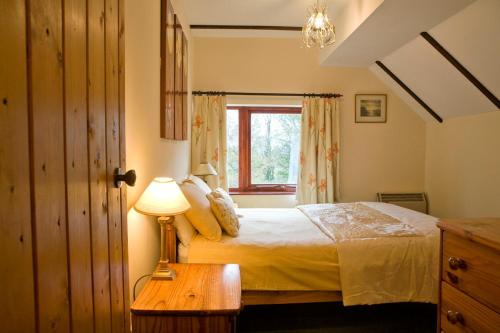 a bedroom with a bed with a lamp and a window at Windrush Cottage, Seven Springs Cottages in Cheltenham