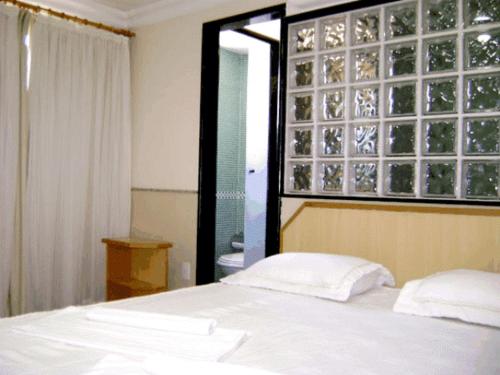 um quarto com uma cama branca e uma janela em Hotel Rosa Mar em Macaé