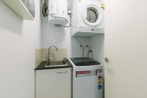 een kleine keuken met een wastafel en een wasmachine bij Darwin City Chic@Kube Apartments in Darwin