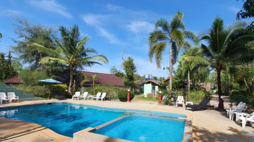 a swimming pool with white chairs and palm trees at Mild Garden View Resort in Ao Nang Beach