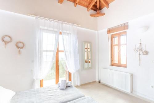 a white bedroom with a bed and a window at Maniatiko Village in Stoupa