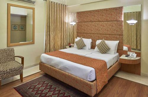 ein Schlafzimmer mit einem Bett, einem Stuhl und einem Spiegel in der Unterkunft Astoria Hotel in Mumbai