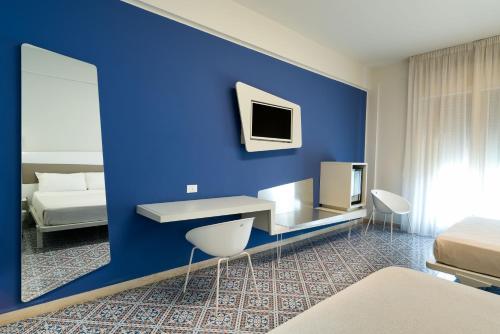 a room with a blue wall with a desk and a bed at Saracen Sands Hotel & Congress Centre - Palermo in Isola delle Femmine