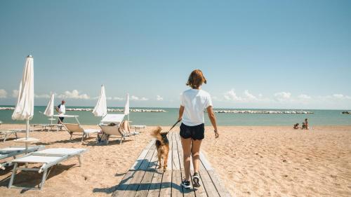 a woman walking a dog on the beach at Natural Village Resort in Porto Potenza Picena