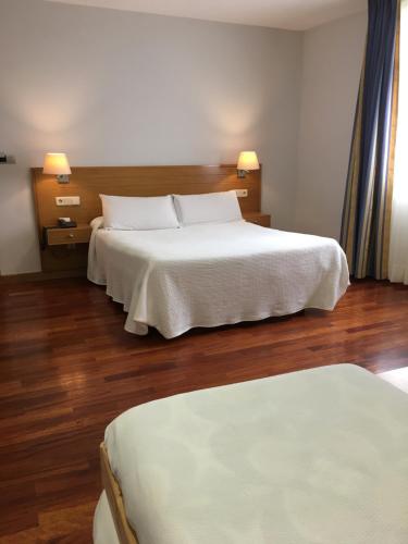Schlafzimmer mit einem Bett mit weißer Bettwäsche und Holzböden in der Unterkunft Hotel Arteixo in Arteixo