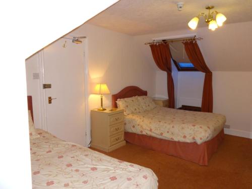 a bedroom with two beds and a lamp on a dresser at Aberdour Guest House in Dumfries