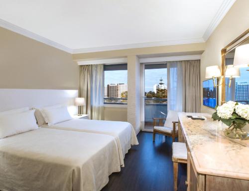 a hotel room with a bed and a desk and windows at Dom Pedro Vilamoura in Vilamoura