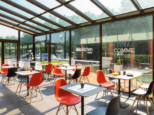un restaurant avec des tables, des chaises et des fenêtres dans l'établissement ibis Paris Marne la Vallee Emerainville, à Émerainville