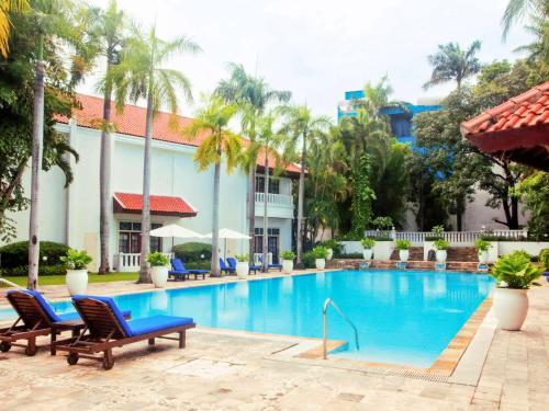 a pool at a resort with chairs and palm trees at Hotel Majapahit Surabaya MGallery in Surabaya