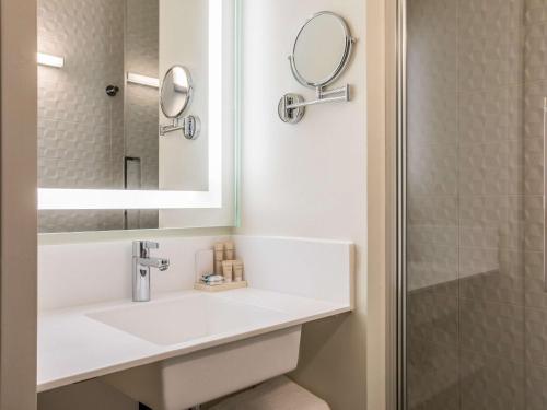 La salle de bains blanche est pourvue d'un lavabo et d'un miroir. dans l'établissement Hôtel Mercure Paris Gennevilliers, à Gennevilliers