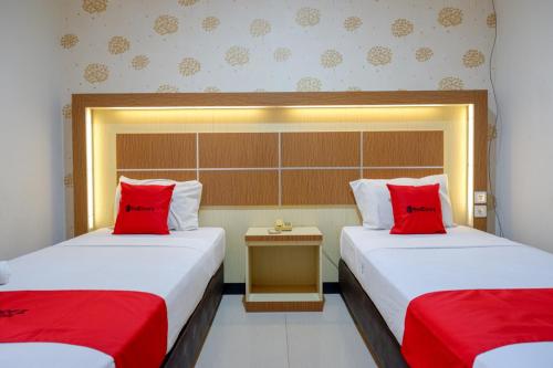 two beds in a hotel room with red pillows at RedDoorz @ Hotel Bumi Palupy in Palu