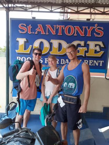 a group of three men standing in front of a sign at St. Antonys Lodge in Cochin