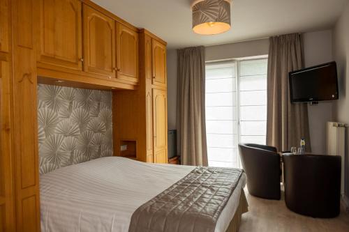 a bedroom with a bed and two chairs and a tv at Logis Beau Séjour in Frahan